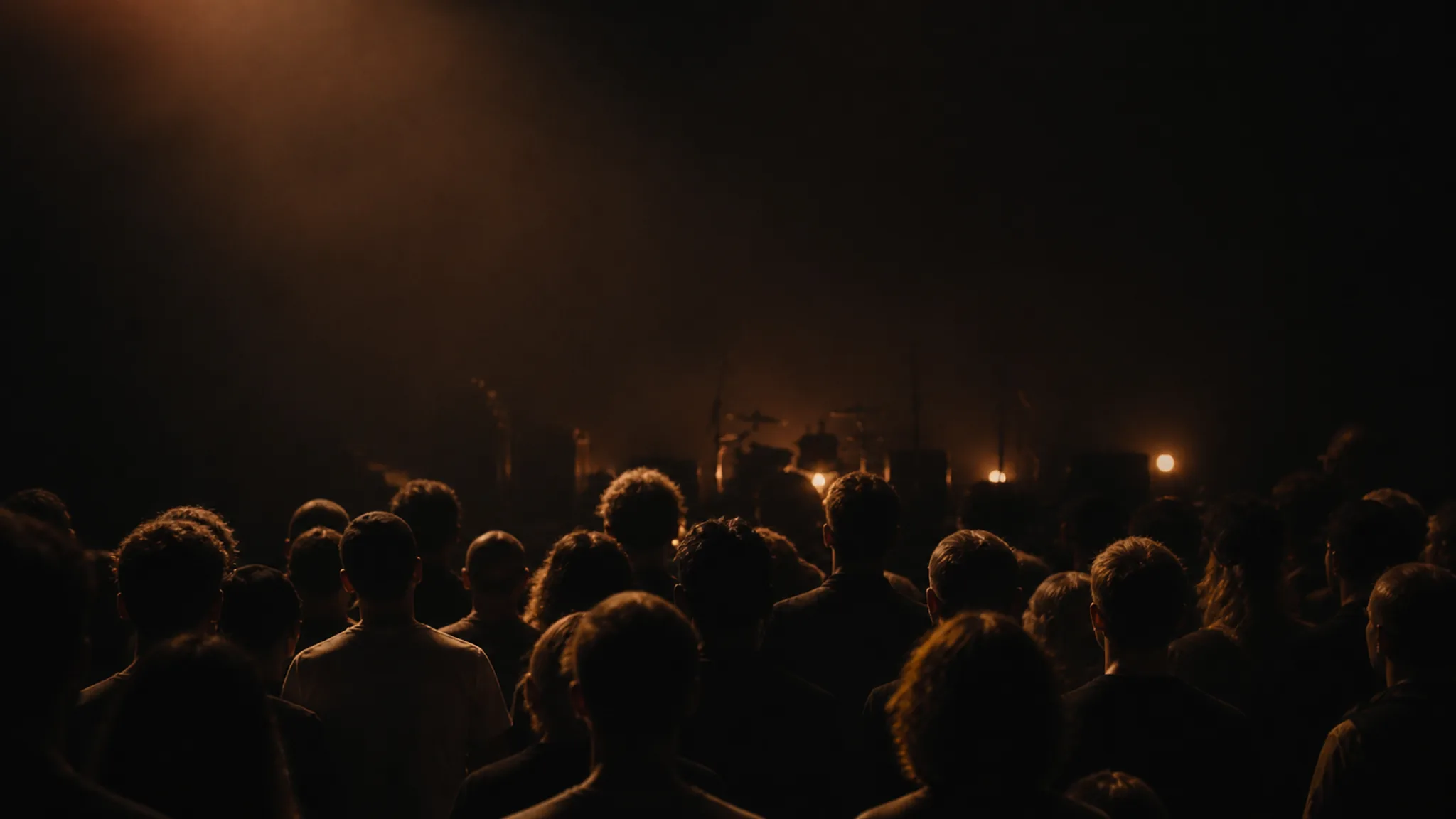 Audience gathered in a dark room before a warmly lit live stage